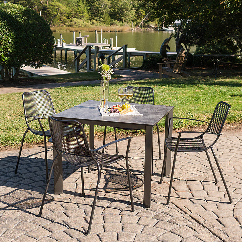 Metro 5-Piece Dining Set with stackable arm chairs and 37-inch weather-resistant HPL dining table outdoors.